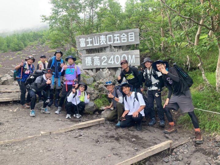 Group of hikers posing beside a wooden sign at Mount Fuji's 5th Station, indicating 2,400 m elevation.