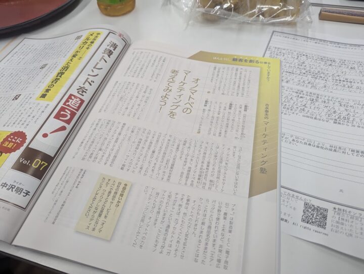 Open Japanese magazine spread on a desk with articles and yellow sidebar highlights, plus other papers nearby.